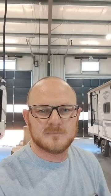 Brandon Beesley in the shop bay, travel trailers parked in the bays behind him, recording an update about winterization season.