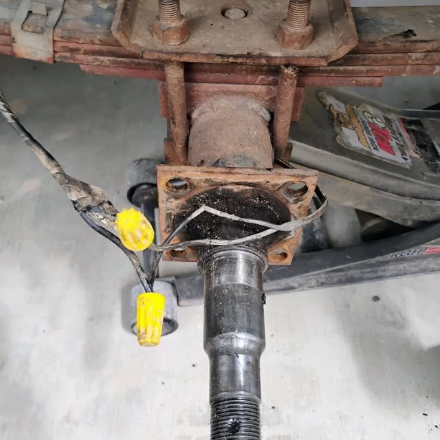 A trailer axle spindle stripped back for new bearings and brakes, the brake wiring connected with fresh butt connectors.