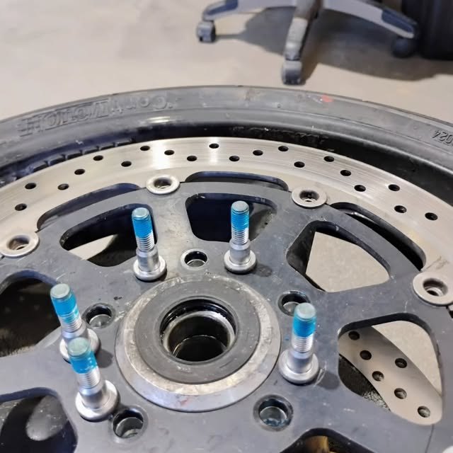 A wheel hub on the bench with its studs freshly treated with blue thread locker, the old compound cleaned off first.