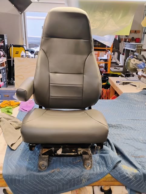 A heavy equipment operator seat freshly recovered in slate grey vinyl, sitting on a moving blanket in the shop.