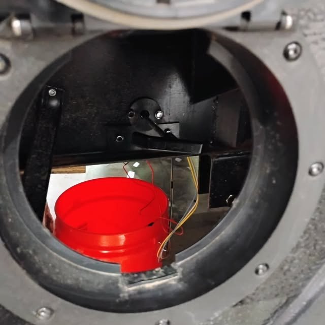 An open access hatch on a travel trailer with a red bucket set under a leaking tank fitting.